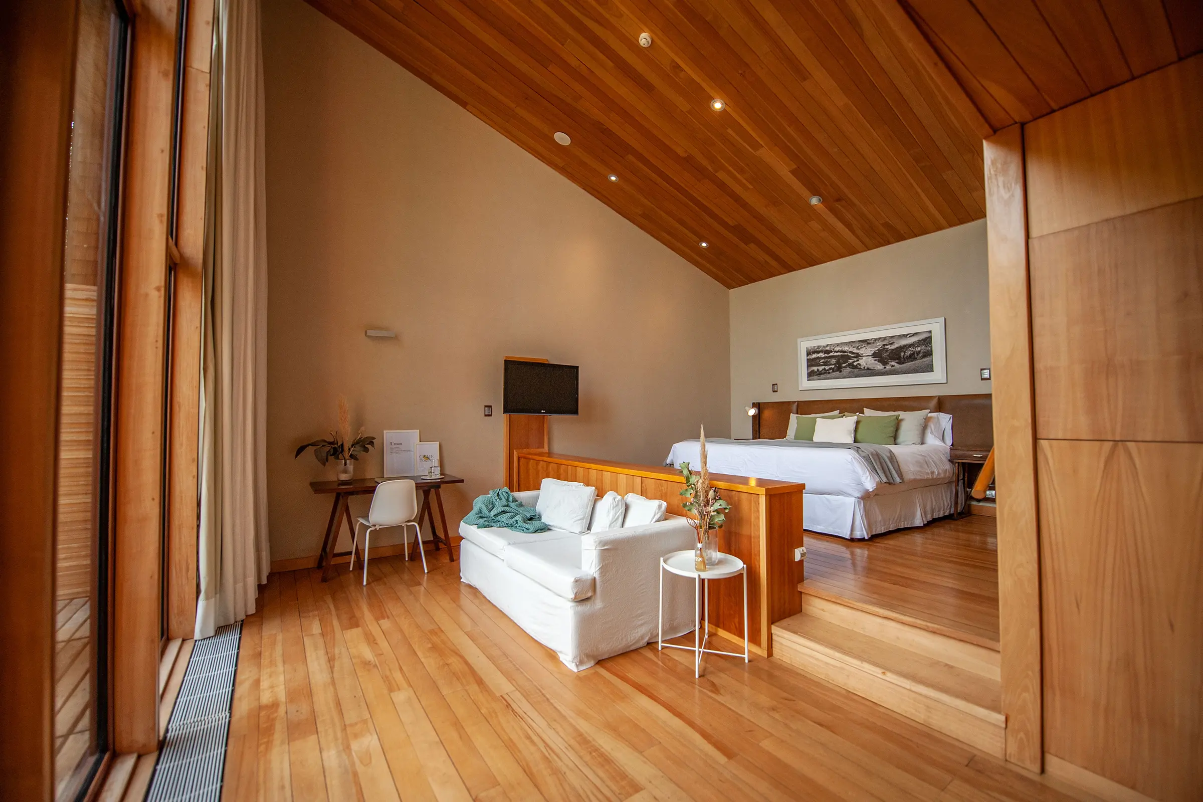 Interior de suite con techo de madera, cama king y living