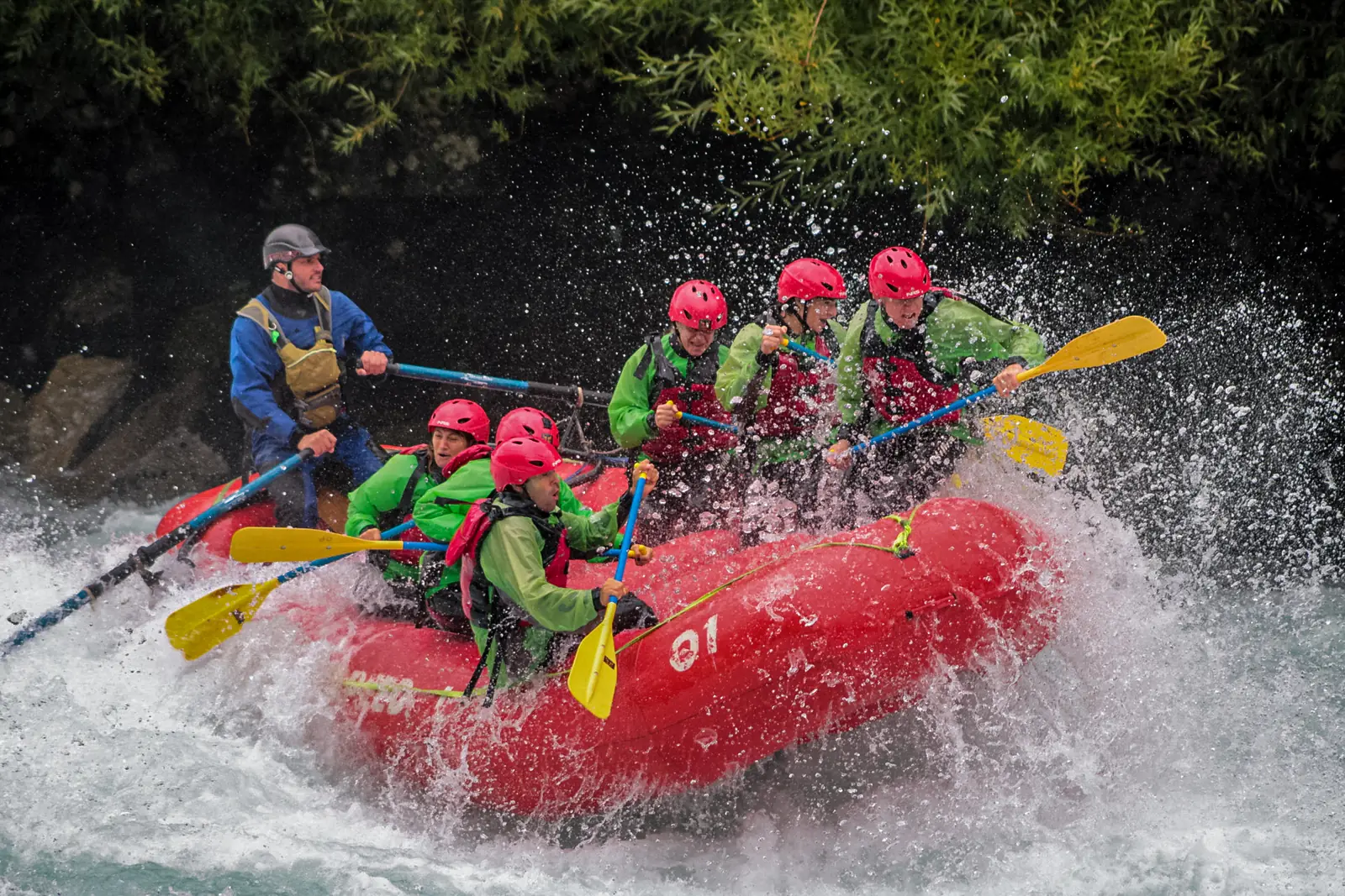 Red raft with six paddlers and a guide punching through a white wave on the Futaleufú River, below the canyon wall