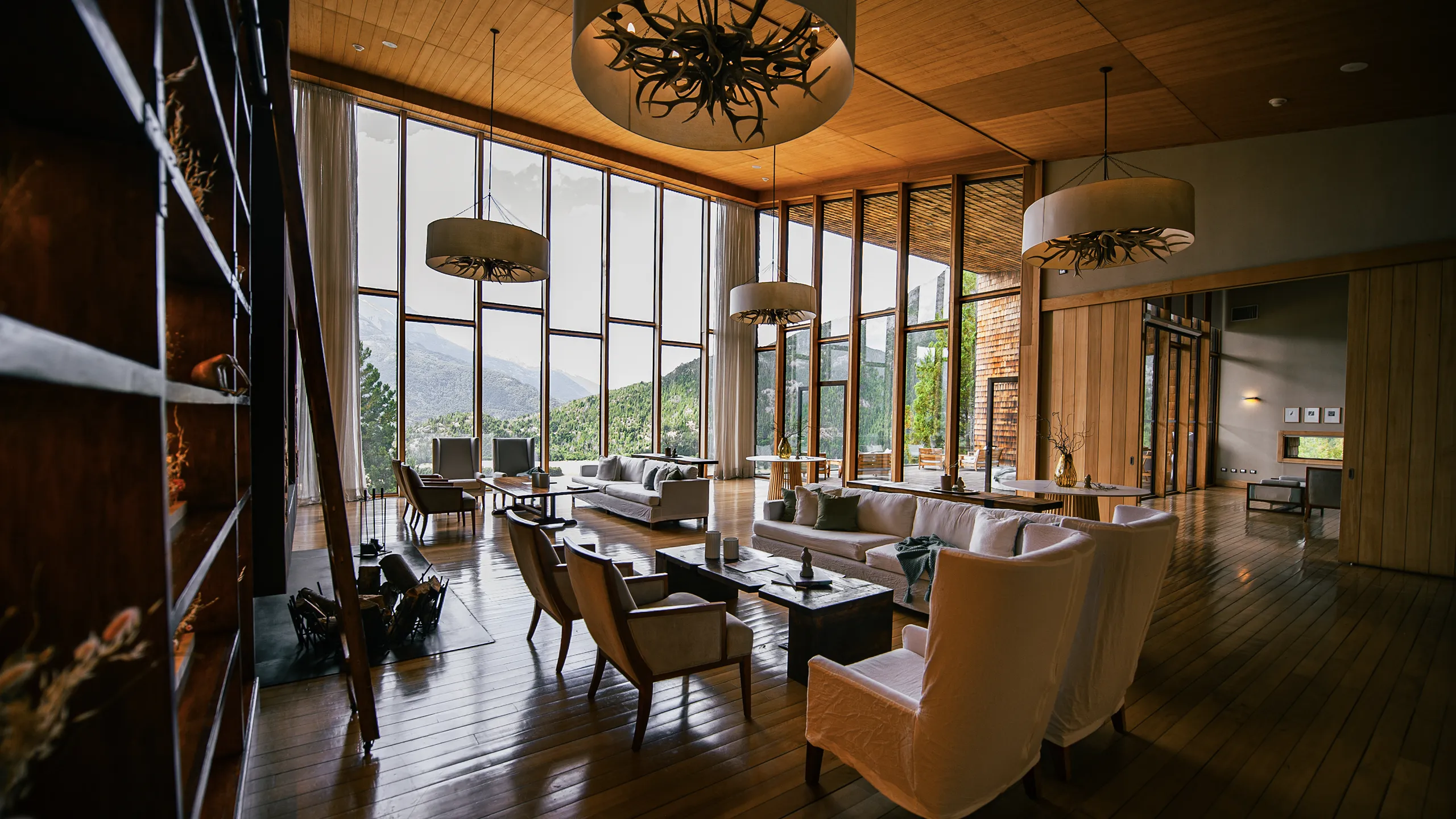 Living del lodge con ventanales del piso al techo, lámparas de astas y vista a la cordillera