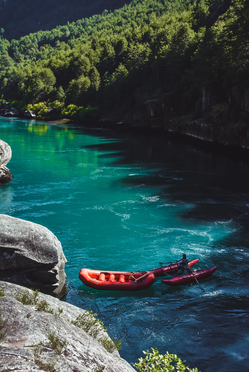 Red rafts in a turquoise pool at the foot of a forested rock cliff on the Futaleufú