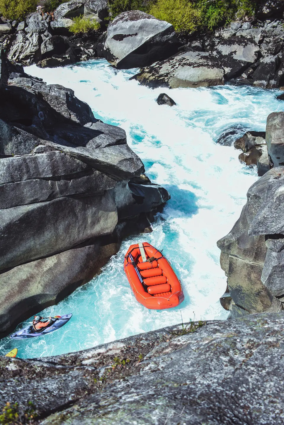 Orange raft dropping through white water between huge granite boulders on the Futaleufú, followed by a kayaker