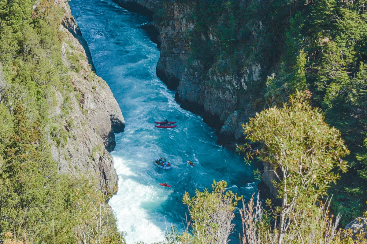 Aerial view of a Futaleufú River canyon, turquoise water between rock walls and forest, with rafts and kayaks heading downstream